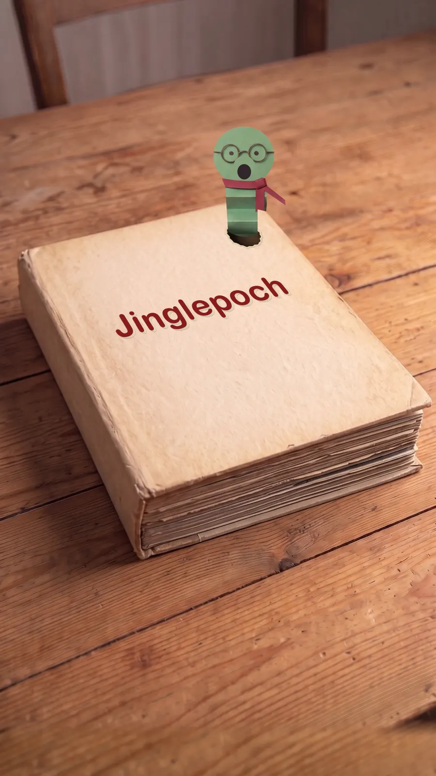 Footnote, a folded-paper bookworm with round glasses, peeking out of the Jinglepoch book.